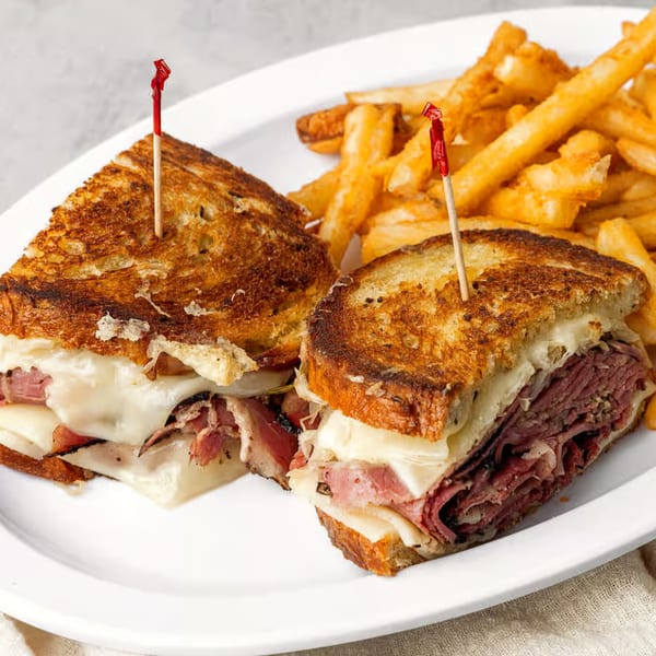 Two halves of a grilled NY Deli Reuben sandwich with fries on a white plate.