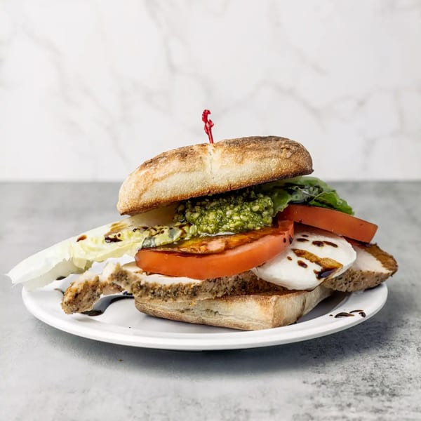 A NY Deli breakfast sandwich with pesto, tomato, mozzarella, and balsamic glaze on a white plate.