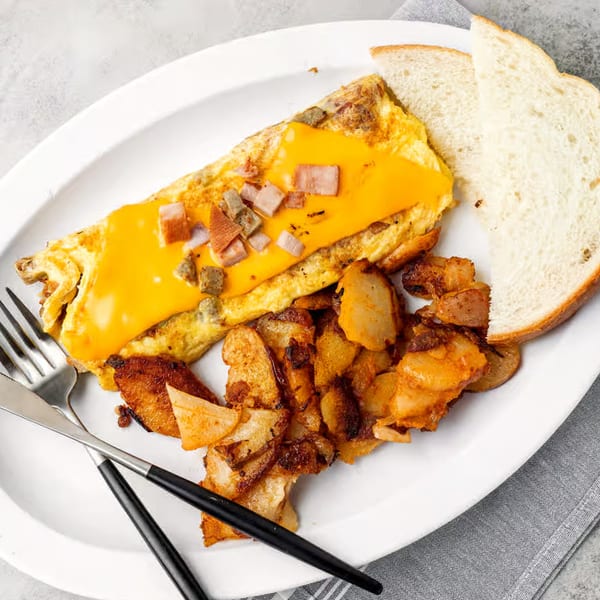 A NY Deli breakfast plate with a cheese and ham omelet, home fries, and white toast.