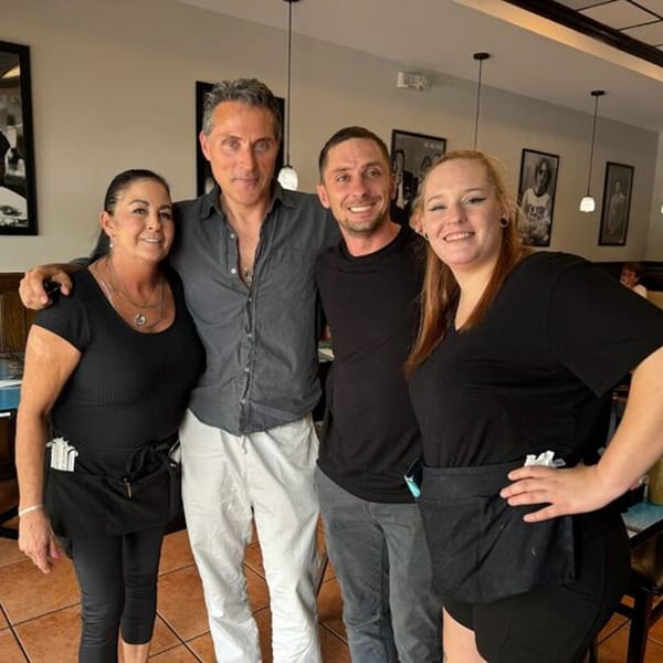 Four smiling NY Deli staff members, two men and two women, pose together in the restaurant.