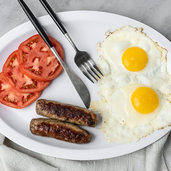 NY Deli breakfast plate with two fried eggs, two sausages, and sliced tomatoes.