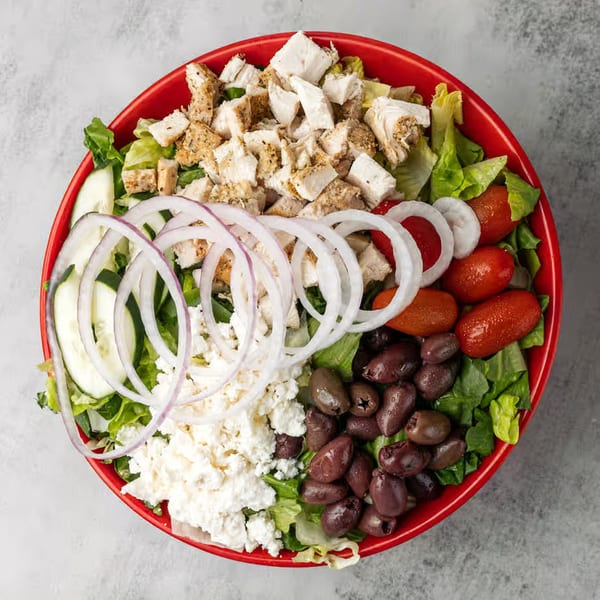 Overhead view of a vibrant salad in a red bowl, featuring chicken, feta, olives, and vegetables.