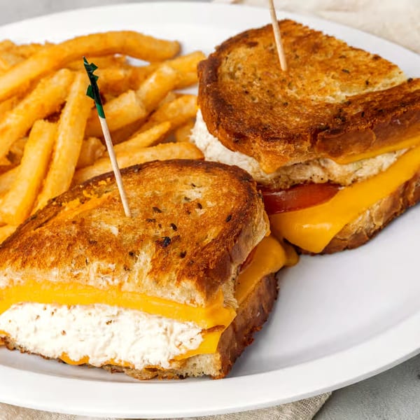 Two grilled cheese sandwiches with tuna salad and fries on a white plate.