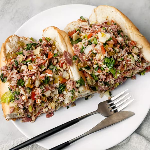 A large NY Deli breakfast sandwich, cut in half, filled with chopped meats, cheese, and vegetables.